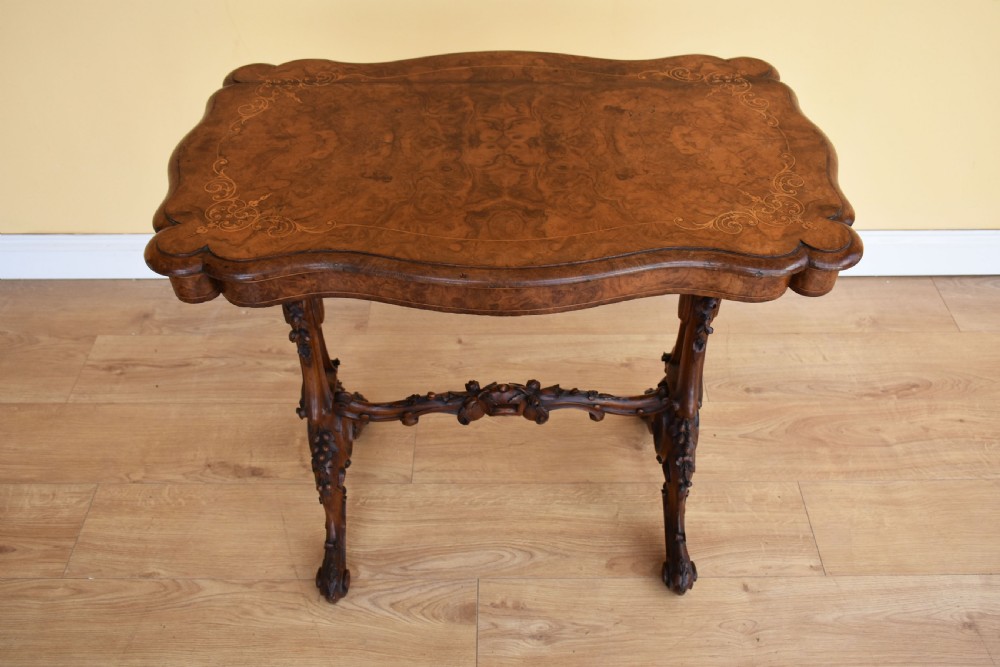 A Victorian burr walnut occasional table featuring a serpentine top with wood inlay, supported by carved legs and a central stretcher. View V