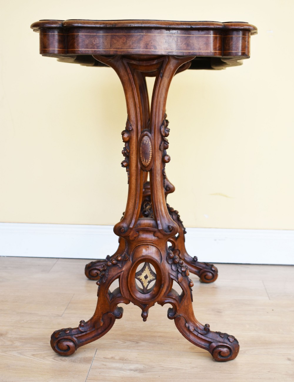 A Victorian burr walnut occasional table featuring a serpentine top with wood inlay, supported by carved legs and a central stretcher. View VI