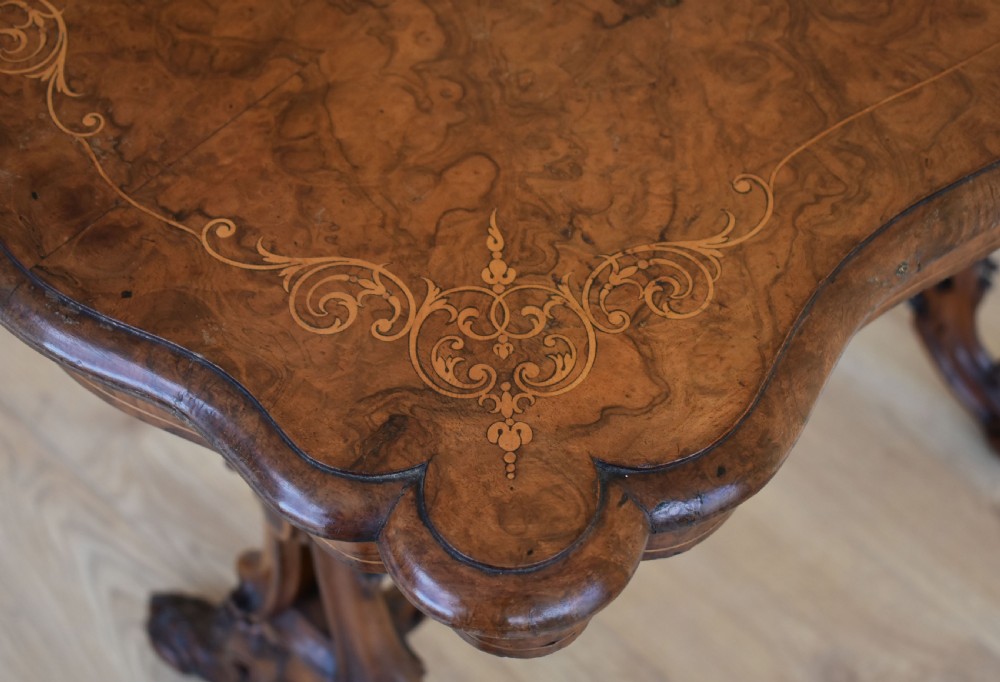 A Victorian burr walnut occasional table featuring a serpentine top with wood inlay, supported by carved legs and a central stretcher. View X