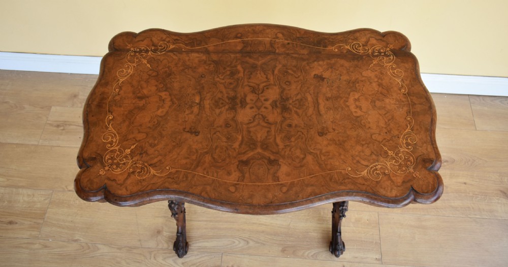 A Victorian burr walnut occasional table featuring a serpentine top with wood inlay, supported by carved legs and a central stretcher. View XI