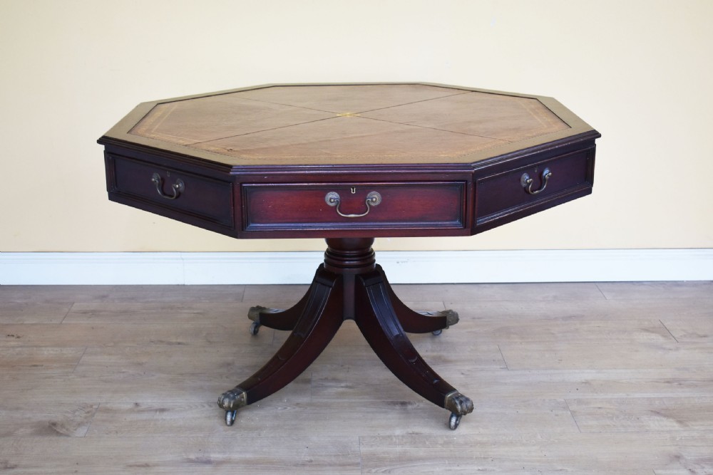 An octagonal Edwardian mahogany drum table featuring a leather inset top, drawers with brass handles, and a central pedestal with four splayed legs on brass castors.