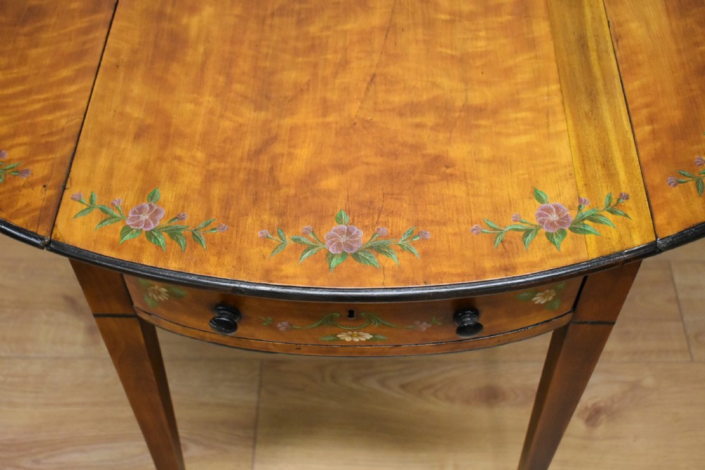An Edwardian oval drop-leaf Pembroke table crafted from mahogany and satinwood, decorated with painted floral motifs and supported on tapered legs with brass castors. View IX