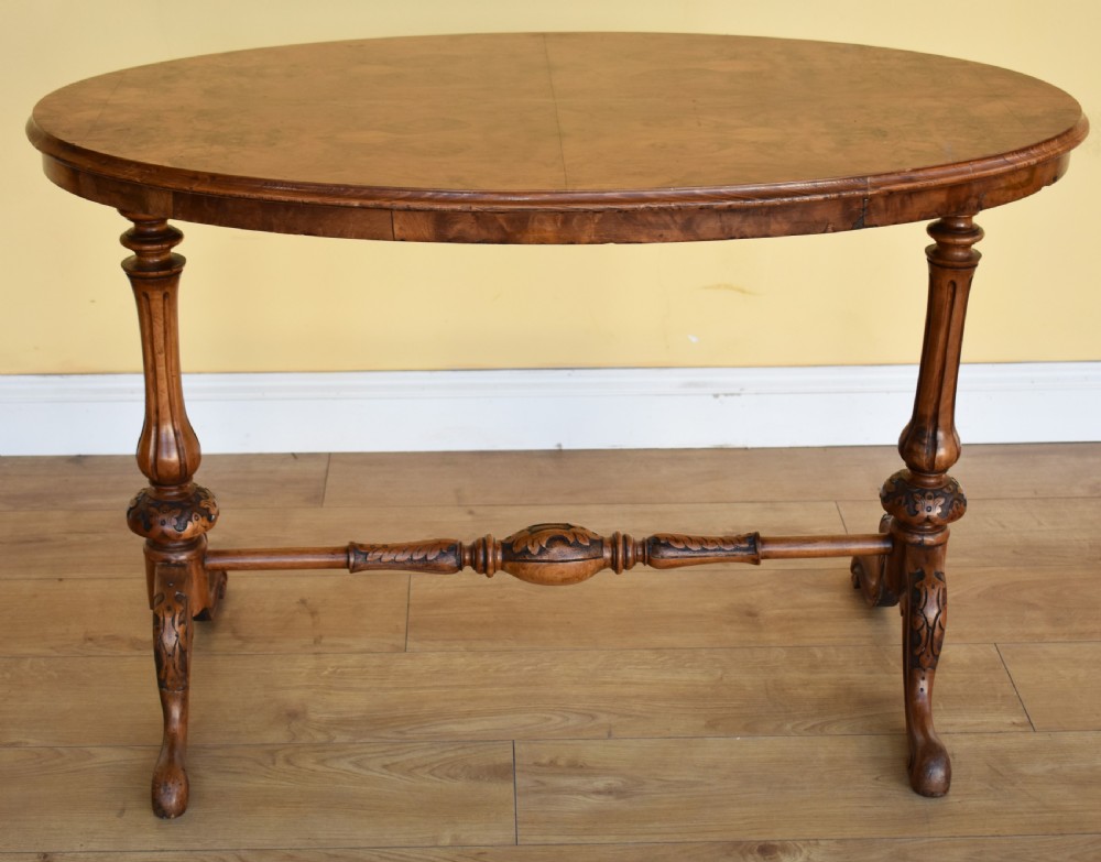 An oval Victorian burr walnut occasional table featuring carved turned uprights, a decorative stretcher, and carved cabriole legs.
