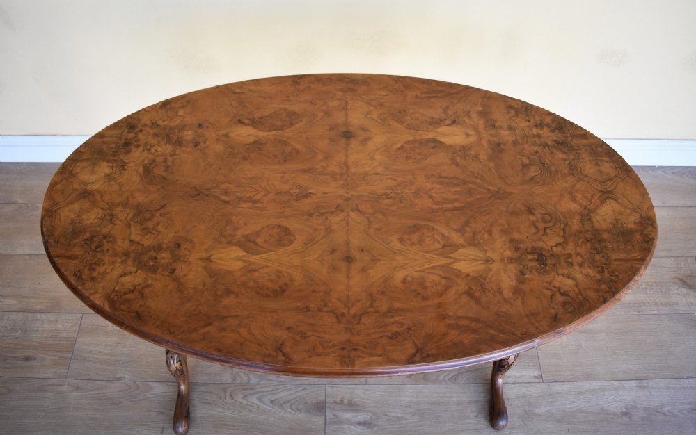 An oval Victorian burr walnut occasional table featuring carved turned uprights, a decorative stretcher, and carved cabriole legs. View II