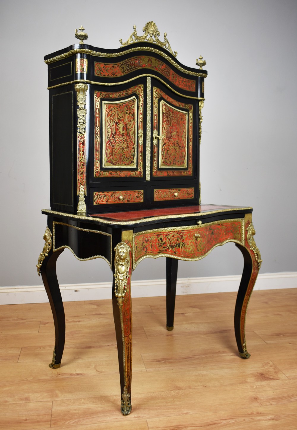 A 19th-century ebonised French bonheur du jour writing desk featuring red tortoiseshell and brass Boulle marquetry, cabriole legs, and gilt-bronze mounts.