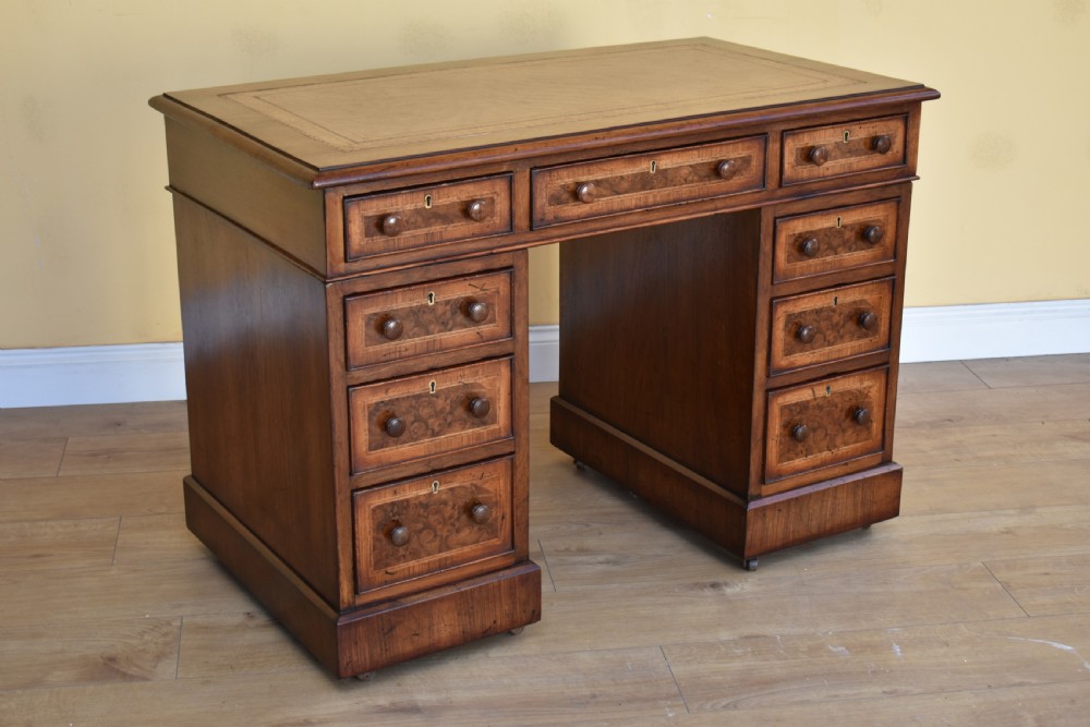A nineteenth-century Victorian pedestal desk crafted from burr walnut featuring nine drawers with turned wooden handles and a leather writing top.