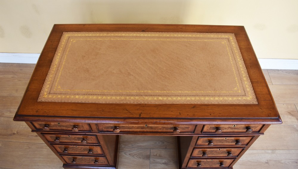 A nineteenth-century Victorian pedestal desk crafted from burr walnut featuring nine drawers with turned wooden handles and a leather writing top. View VI