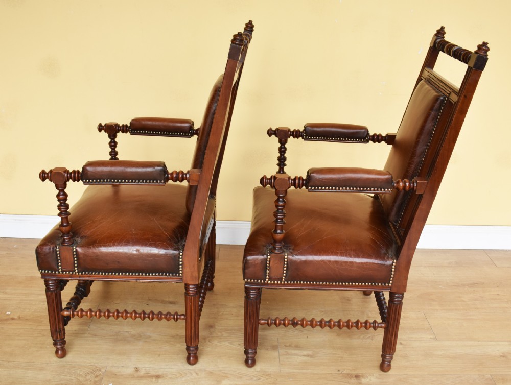 A pair of 19th-century Victorian walnut Gothic Revival armchairs featuring bobbin-turned stretchers and warm brown leather upholstery with brass studding. View V