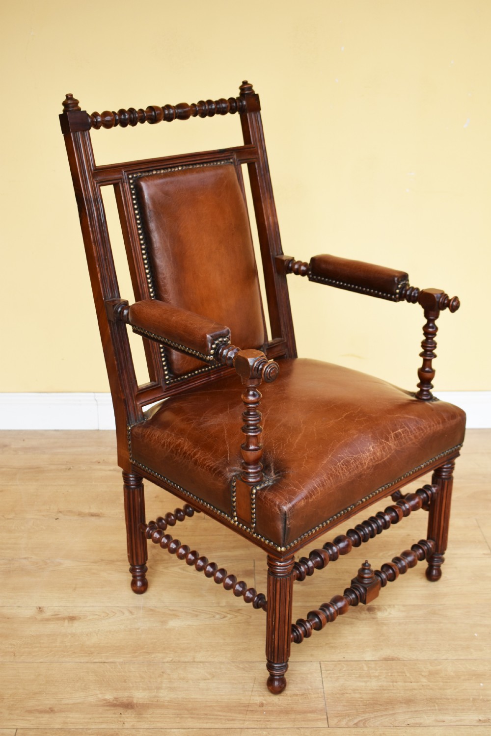 A pair of 19th-century Victorian walnut Gothic Revival armchairs featuring bobbin-turned stretchers and warm brown leather upholstery with brass studding. View VI