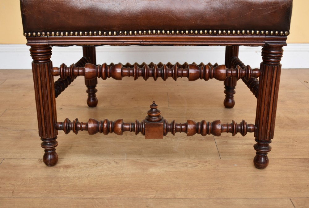 A pair of 19th-century Victorian walnut Gothic Revival armchairs featuring bobbin-turned stretchers and warm brown leather upholstery with brass studding. View X