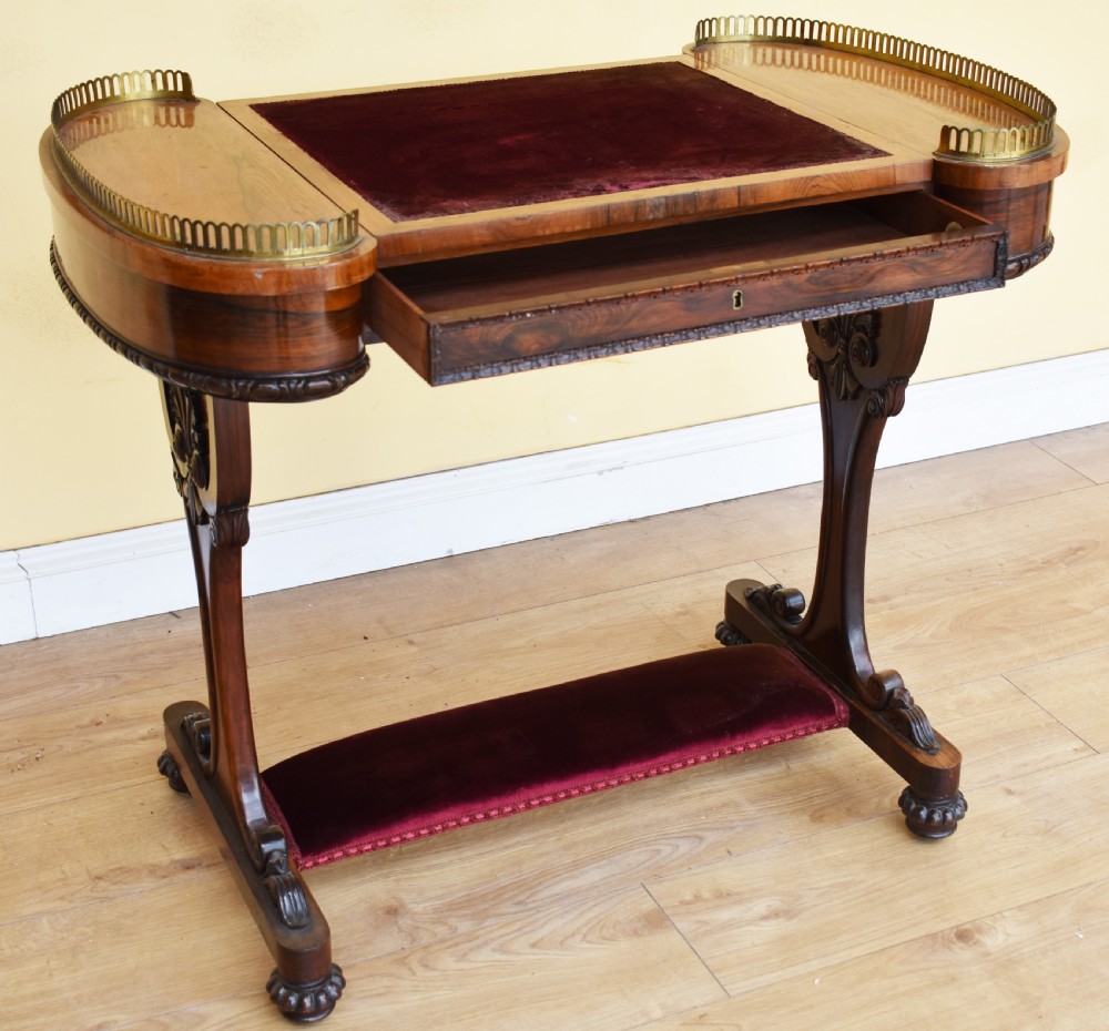 A 19th-century William IV rosewood writing table featuring an adjustable velvet-covered reading slope flanked by brass gallery rails on carved pedestal supports. View X