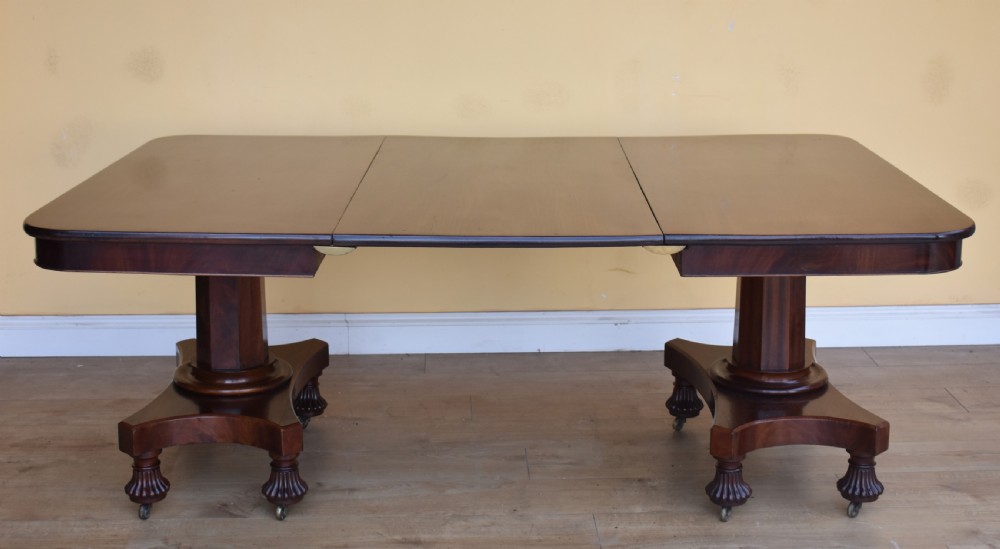 A 19th-century Regency mahogany extending dining table with twin octagonal pedestals, concave bases, reeded feet, and brass castors.