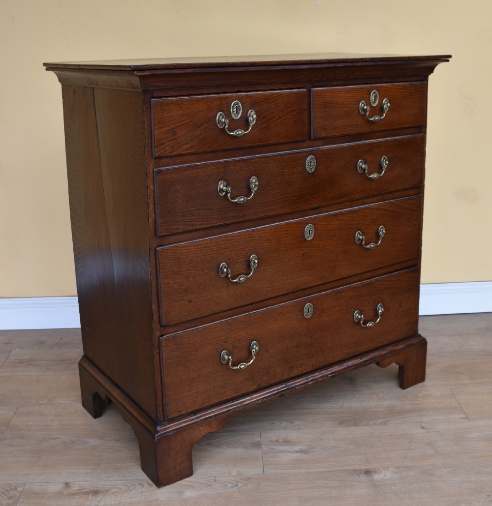 An 18th-century George III oak chest of drawers featuring a two over three drawer arrangement with brass handles and bracket feet.