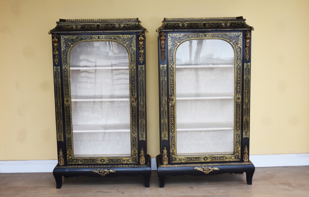 A pair of 19th-century ebonised display cabinets decorated with intricate brass Boulle marquetry, glazed arched doors, and gilt-bronze mounts.