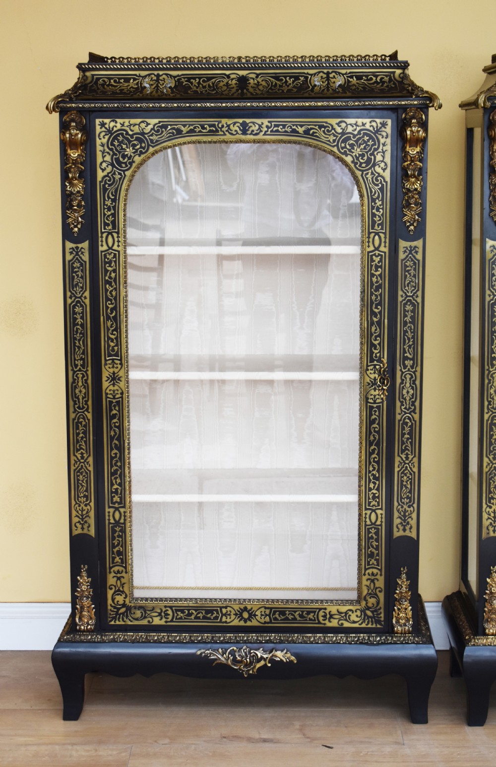 A pair of 19th-century ebonised display cabinets decorated with intricate brass Boulle marquetry, glazed arched doors, and gilt-bronze mounts. View II