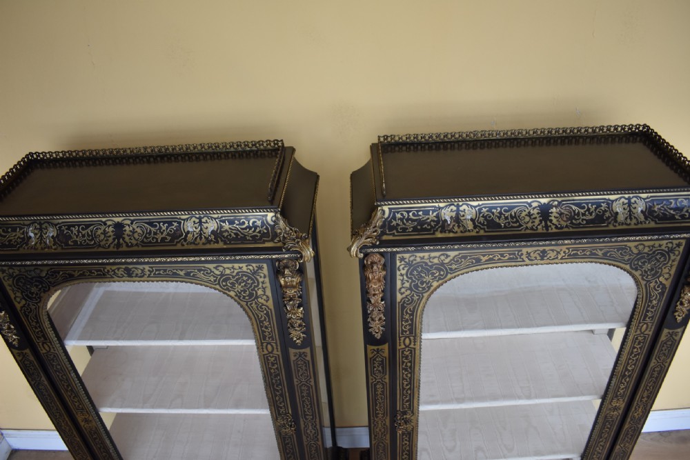 A pair of 19th-century ebonised display cabinets decorated with intricate brass Boulle marquetry, glazed arched doors, and gilt-bronze mounts. View IX