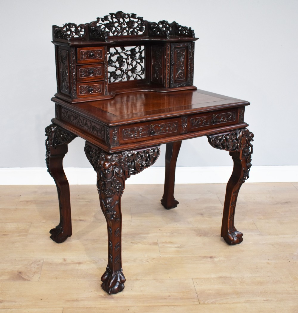 A 19th-century Chinese carved padouk wood desk featuring an intricate openwork gallery superstructure, frieze drawers, and cabriole legs ending in claw feet.