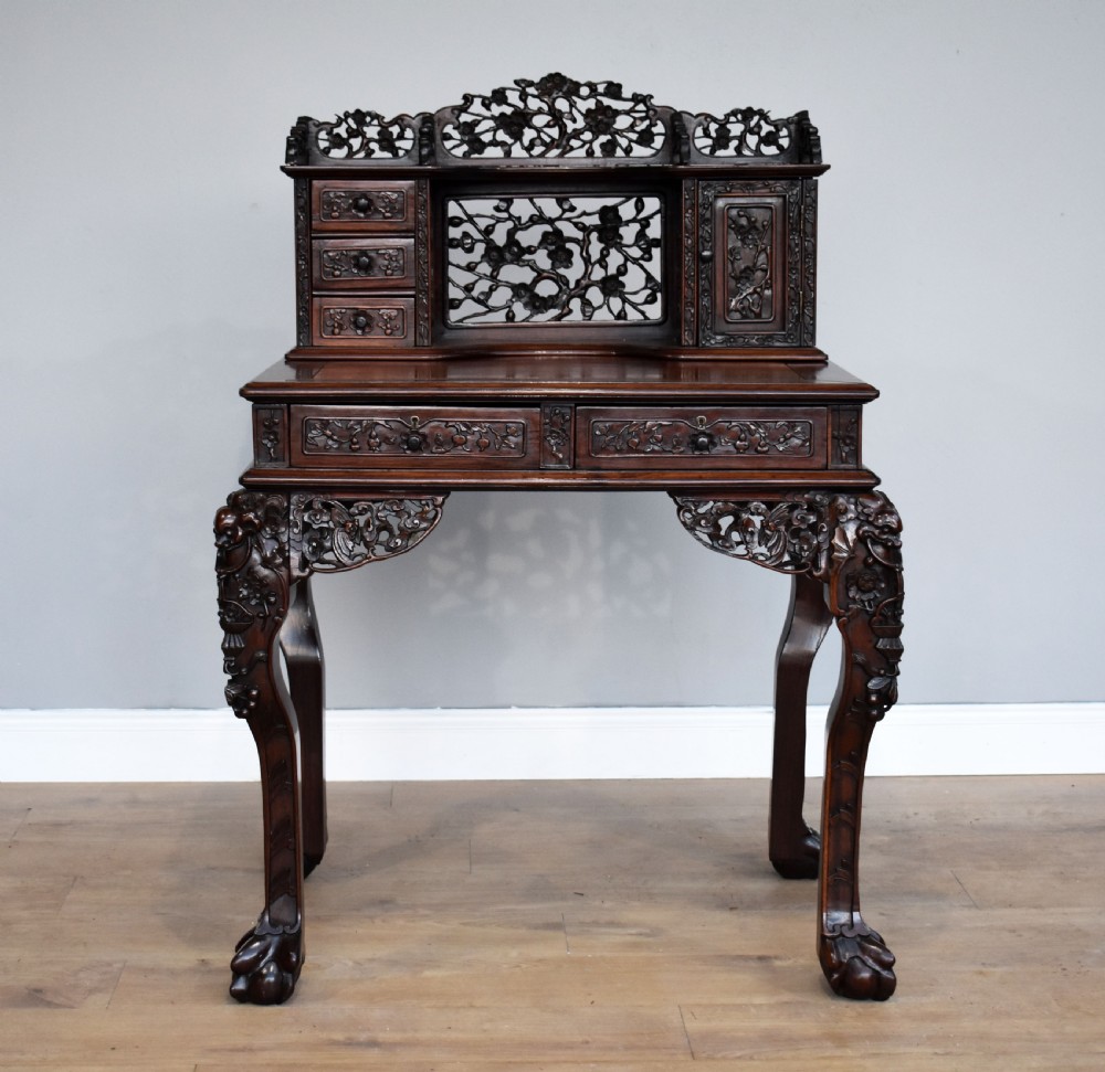 A 19th-century Chinese carved padouk wood desk featuring an intricate openwork gallery superstructure, frieze drawers, and cabriole legs ending in claw feet. View II