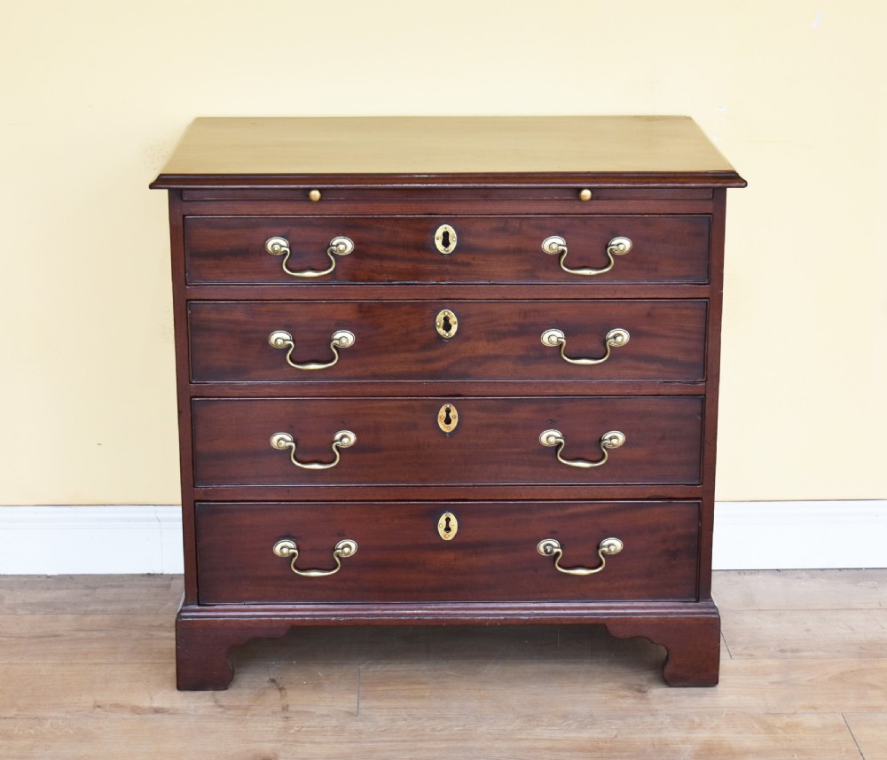A George III mahogany chest of drawers featuring four graduated drawers, brass swan-neck handles, keyhole escutcheons, a brushing slide, and bracket feet. View II