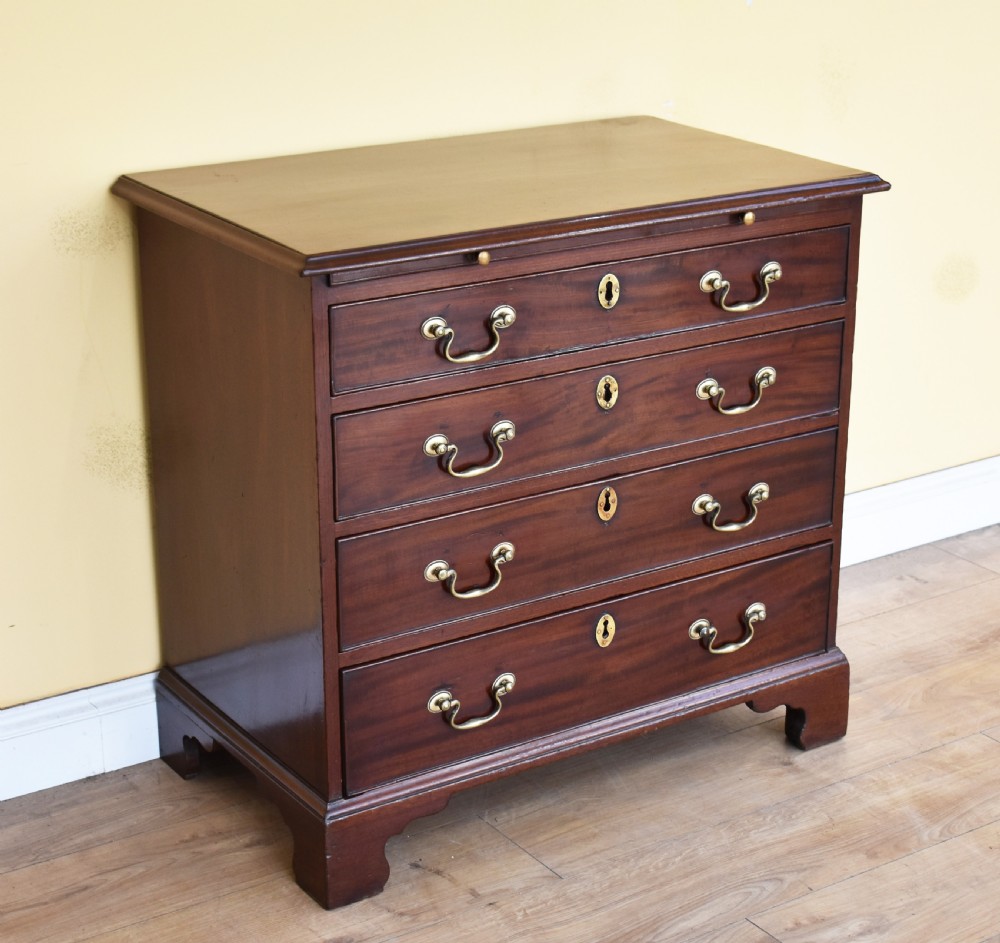 A George III mahogany chest of drawers featuring four graduated drawers, brass swan-neck handles, keyhole escutcheons, a brushing slide, and bracket feet.