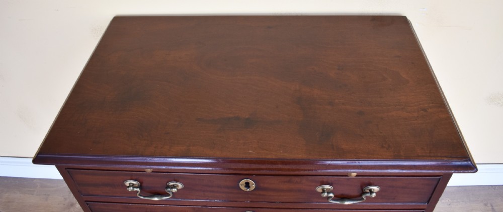 A George III mahogany chest of drawers featuring four graduated drawers, brass swan-neck handles, keyhole escutcheons, a brushing slide, and bracket feet. View III