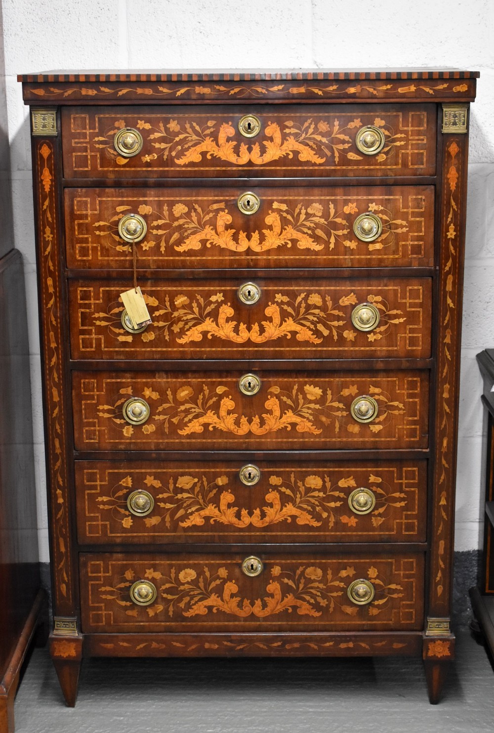 An 18th-century Dutch marquetry chest of six drawers featuring elaborate floral wood inlays and brass ring handles.