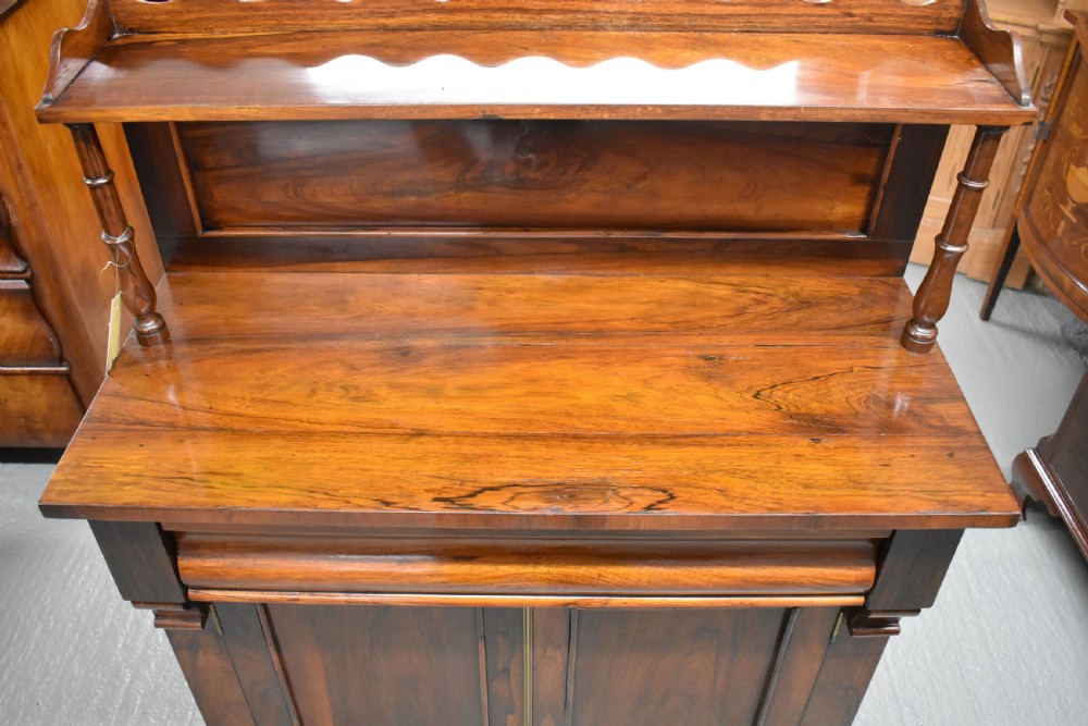 A Victorian rosewood chiffonier cabinet featuring twin panelled doors, a long frieze drawer, an upper gallery shelf with turned supports, and a solid plinth base. View V