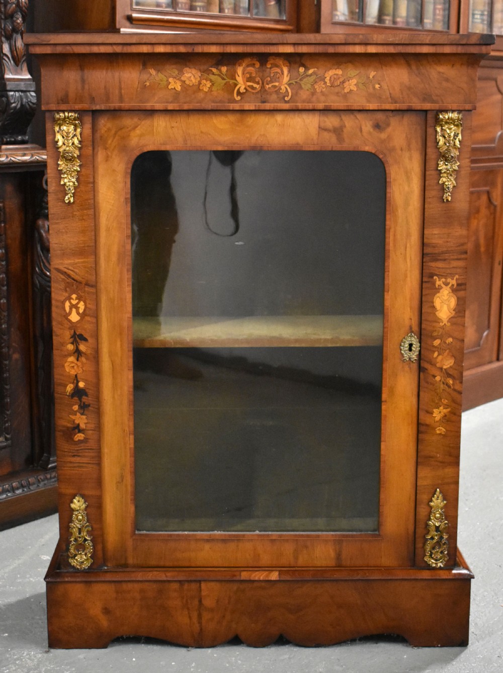 A Victorian walnut pier cabinet with a single glazed door, floral marquetry inlay, and gilt ormolu mounts.