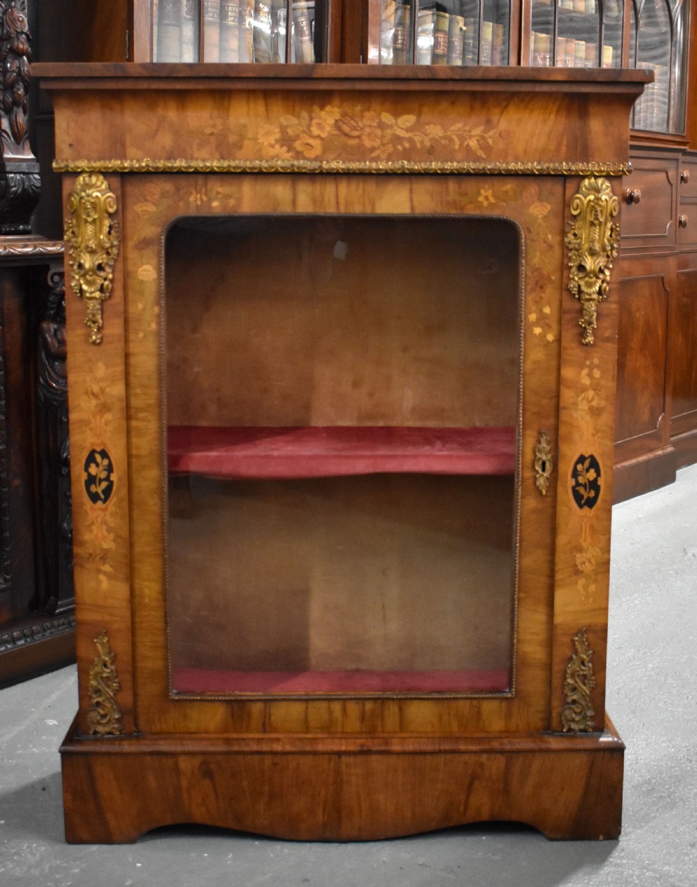 A Victorian walnut pier cabinet featuring floral marquetry inlays, decorative gilt ormolu mounts, and a glass door opening to velvet-lined shelves.