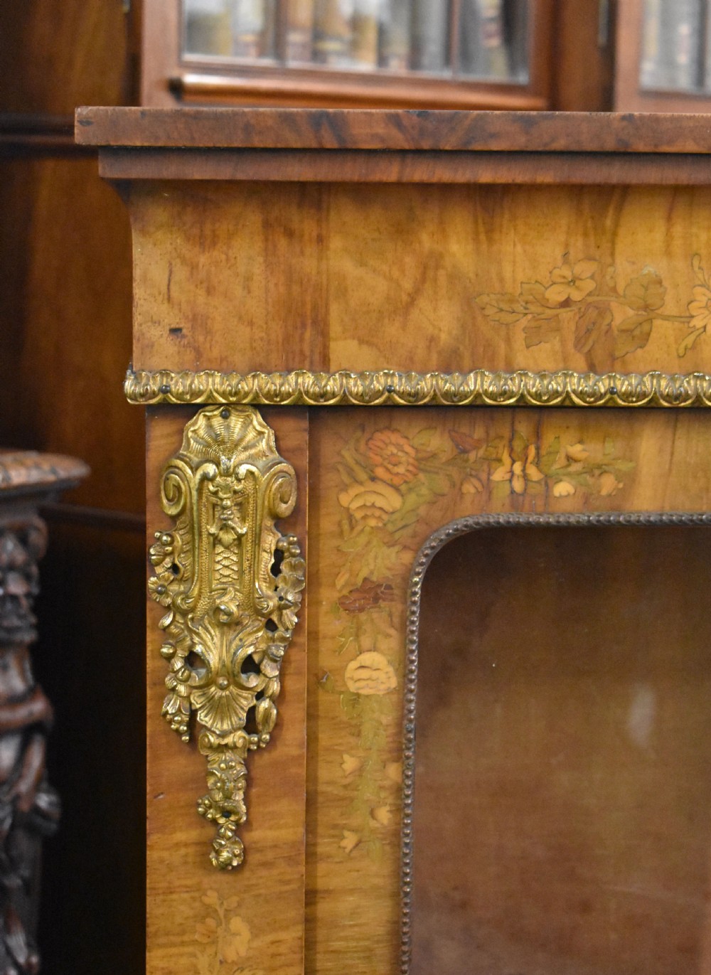A Victorian walnut pier cabinet featuring floral marquetry inlays, decorative gilt ormolu mounts, and a glass door opening to velvet-lined shelves. View V
