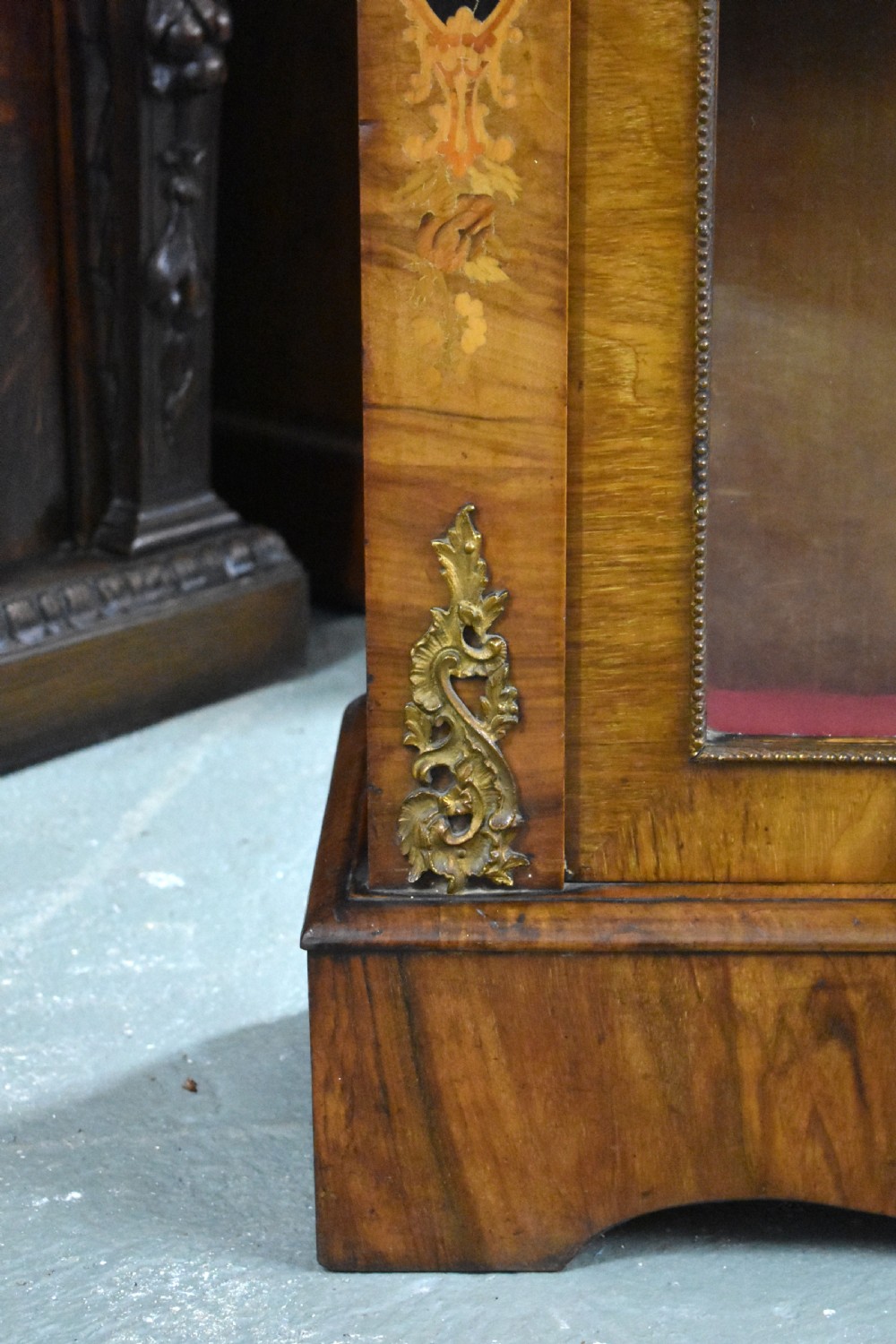 A Victorian walnut pier cabinet featuring floral marquetry inlays, decorative gilt ormolu mounts, and a glass door opening to velvet-lined shelves. View VII