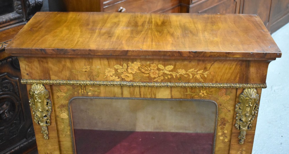 A Victorian walnut pier cabinet featuring floral marquetry inlays, decorative gilt ormolu mounts, and a glass door opening to velvet-lined shelves. View VIII