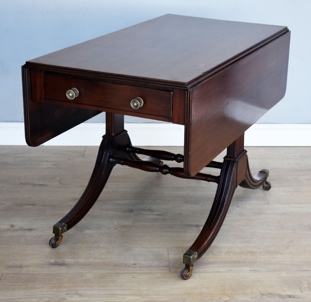 A Regency mahogany Pembroke table featuring drop-leaf sides, a front drawer with brass knobs, reeded splayed legs, and brass castors.