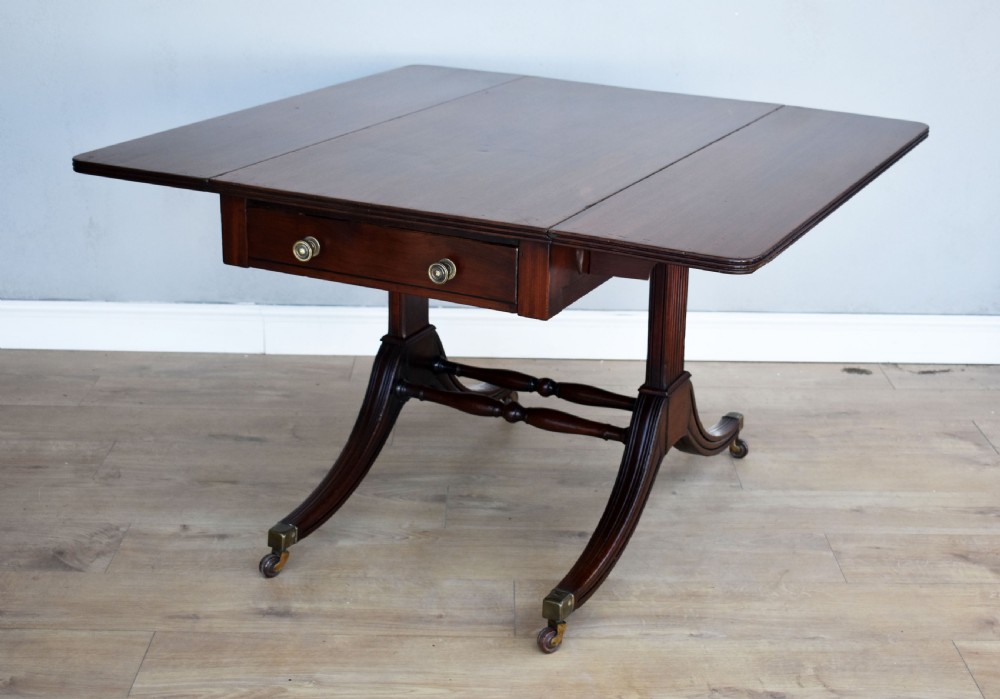 A Regency mahogany Pembroke table featuring drop-leaf sides, a front drawer with brass knobs, reeded splayed legs, and brass castors. View II