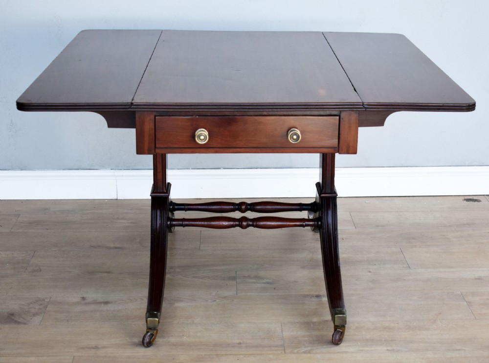 A Regency mahogany Pembroke table featuring drop-leaf sides, a front drawer with brass knobs, reeded splayed legs, and brass castors. View III