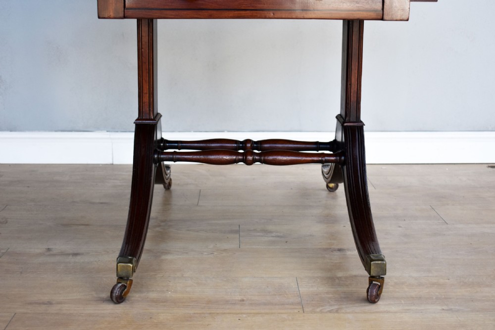 A Regency mahogany Pembroke table featuring drop-leaf sides, a front drawer with brass knobs, reeded splayed legs, and brass castors. View V