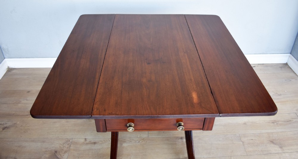A Regency mahogany Pembroke table featuring drop-leaf sides, a front drawer with brass knobs, reeded splayed legs, and brass castors. View VI
