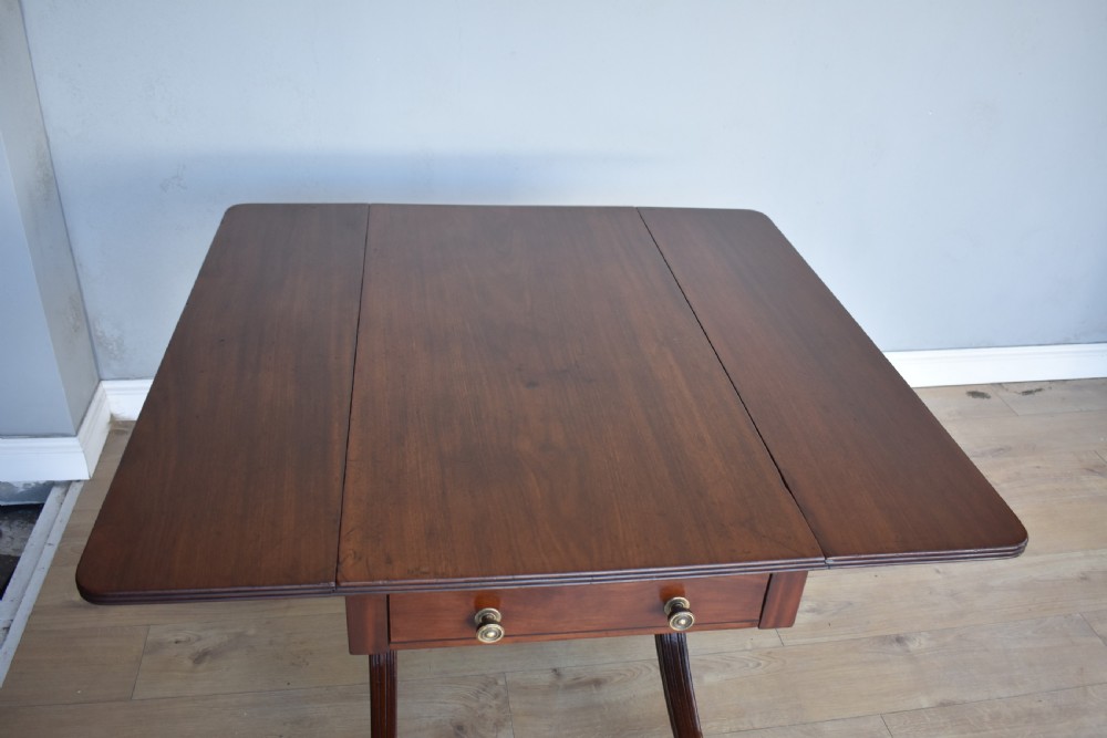 A Regency mahogany Pembroke table featuring drop-leaf sides, a front drawer with brass knobs, reeded splayed legs, and brass castors. View VII