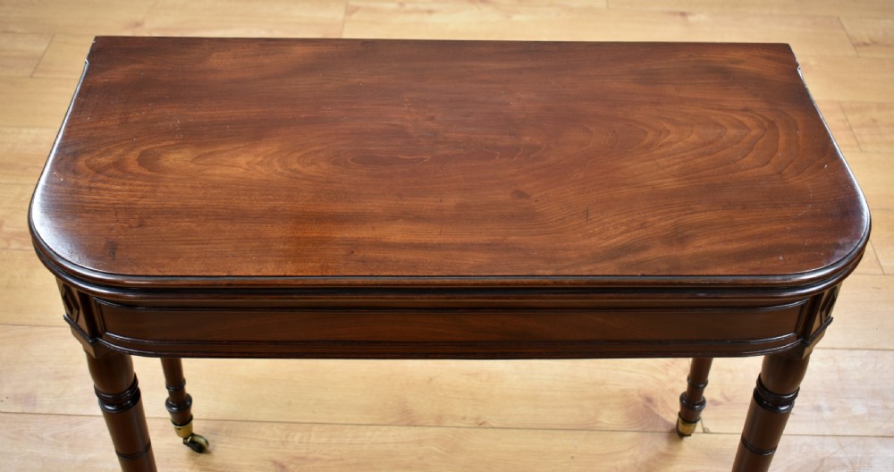 A Georgian dark mahogany fold-over tea table featuring turned reeded legs with brass castors and frieze corner inlays. View II