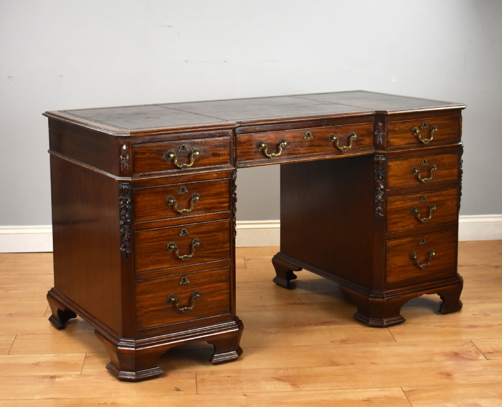 A 19th-century Chippendale style mahogany pedestal desk with a three-section leather inset top, nine drawers, brass handles, and carved pilasters.