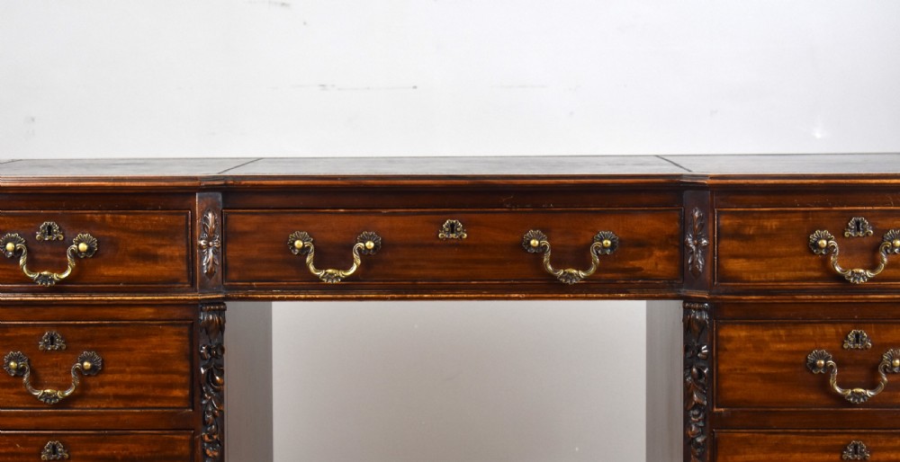 A 19th-century Chippendale style mahogany pedestal desk with a three-section leather inset top, nine drawers, brass handles, and carved pilasters. View IV