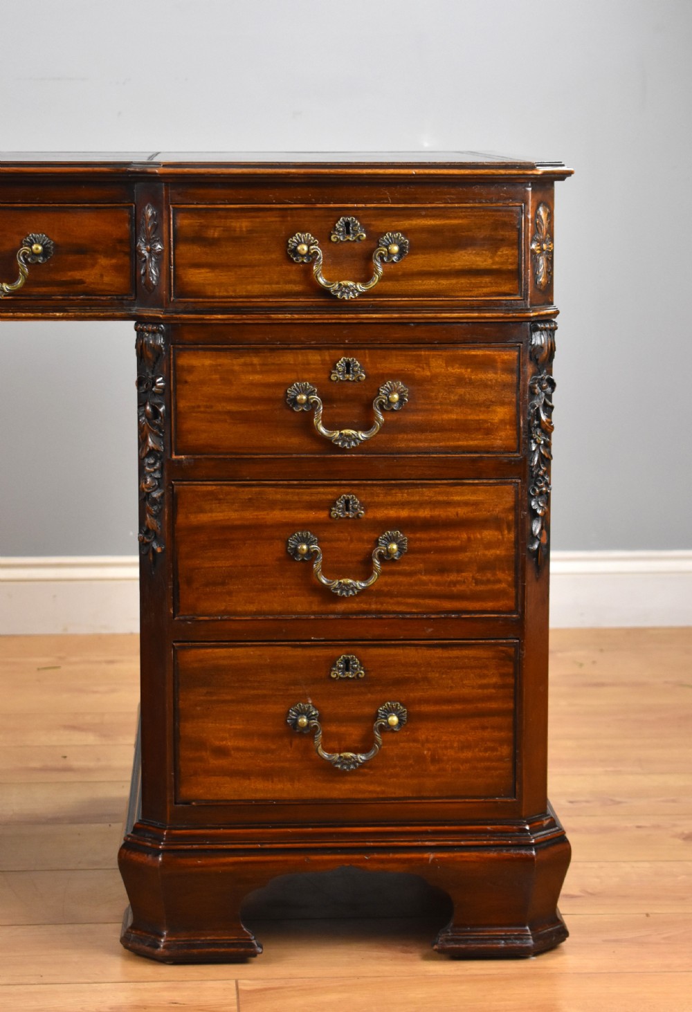 A 19th-century Chippendale style mahogany pedestal desk with a three-section leather inset top, nine drawers, brass handles, and carved pilasters. View V