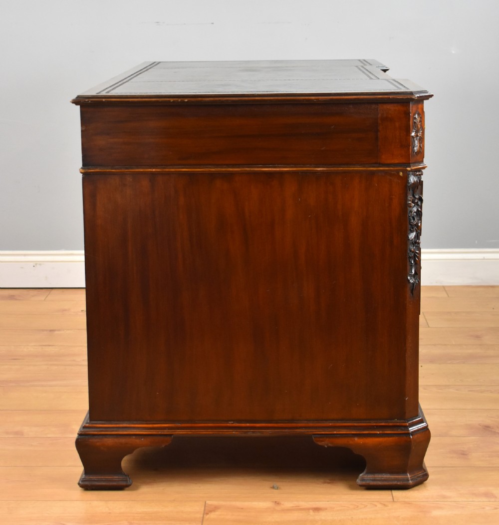 A 19th-century Chippendale style mahogany pedestal desk with a three-section leather inset top, nine drawers, brass handles, and carved pilasters. View VI