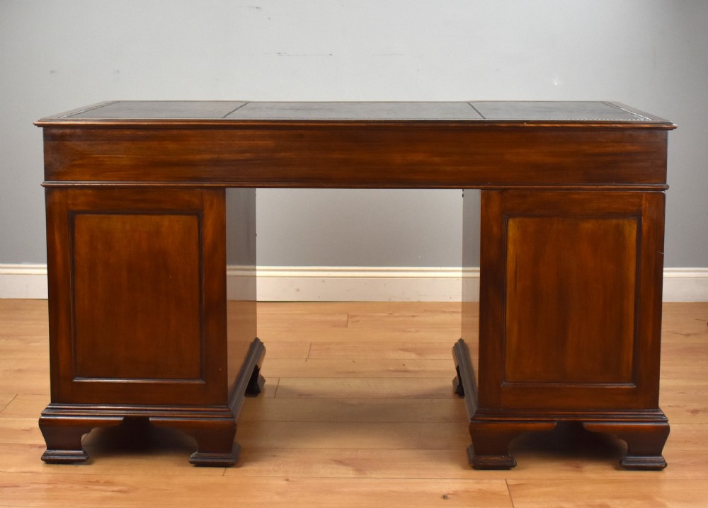 A 19th-century Chippendale style mahogany pedestal desk with a three-section leather inset top, nine drawers, brass handles, and carved pilasters. View VII