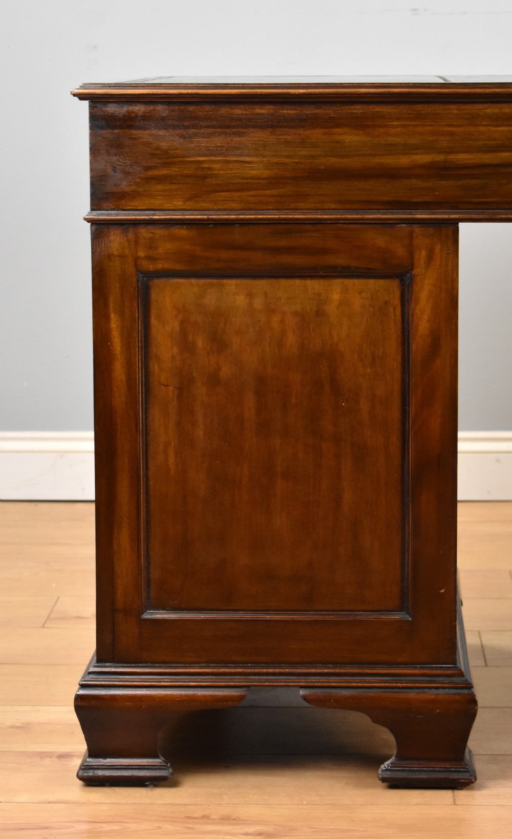 A 19th-century Chippendale style mahogany pedestal desk with a three-section leather inset top, nine drawers, brass handles, and carved pilasters. View IX