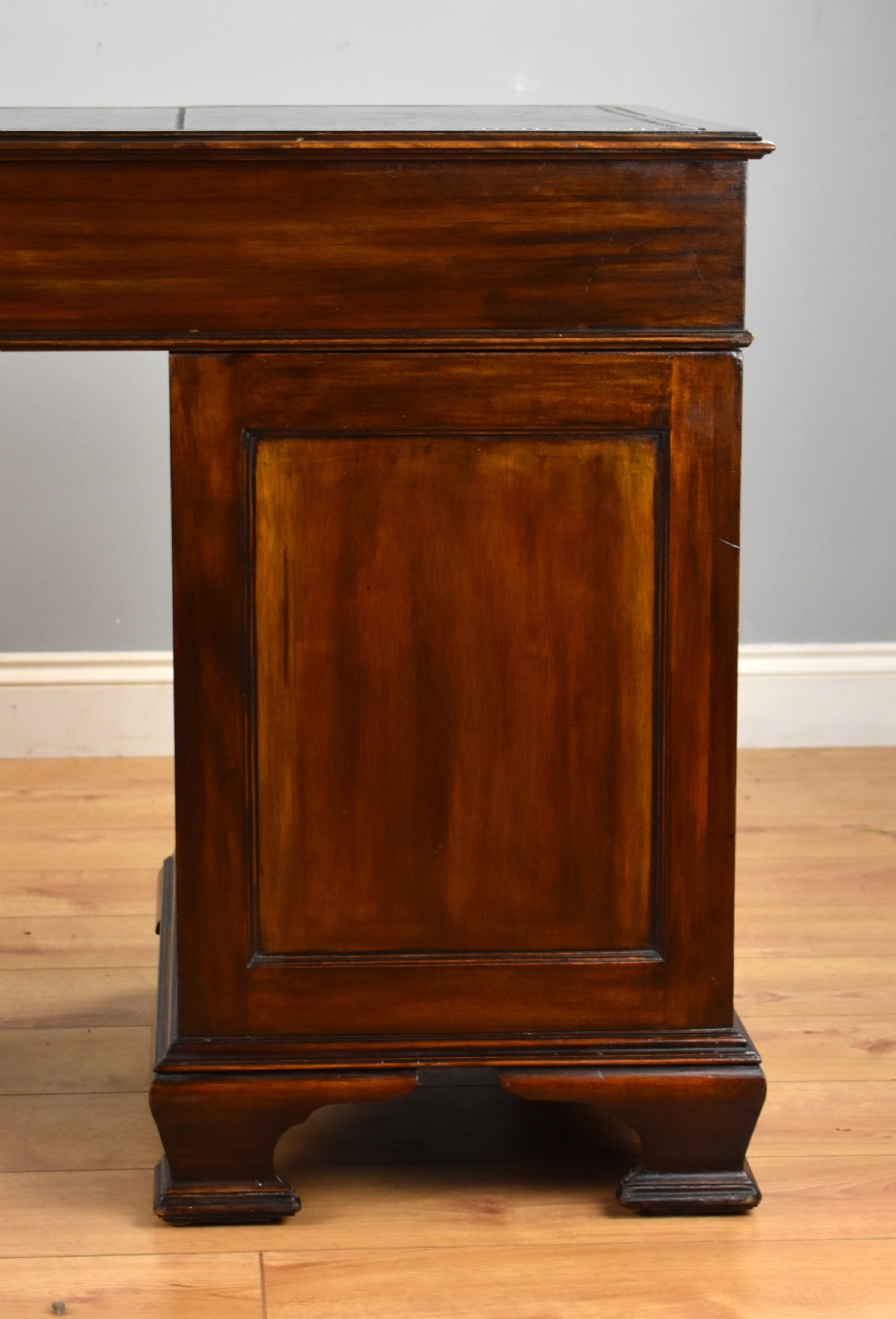 A 19th-century Chippendale style mahogany pedestal desk with a three-section leather inset top, nine drawers, brass handles, and carved pilasters. View X