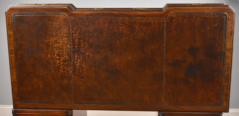 A 19th-century Chippendale style mahogany pedestal desk with a three-section leather inset top, nine drawers, brass handles, and carved pilasters. View XI