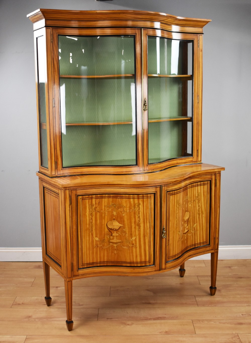 A 19th-century satinwood display cabinet featuring a serpentine glazed upper section and inlaid lower cupboard doors.