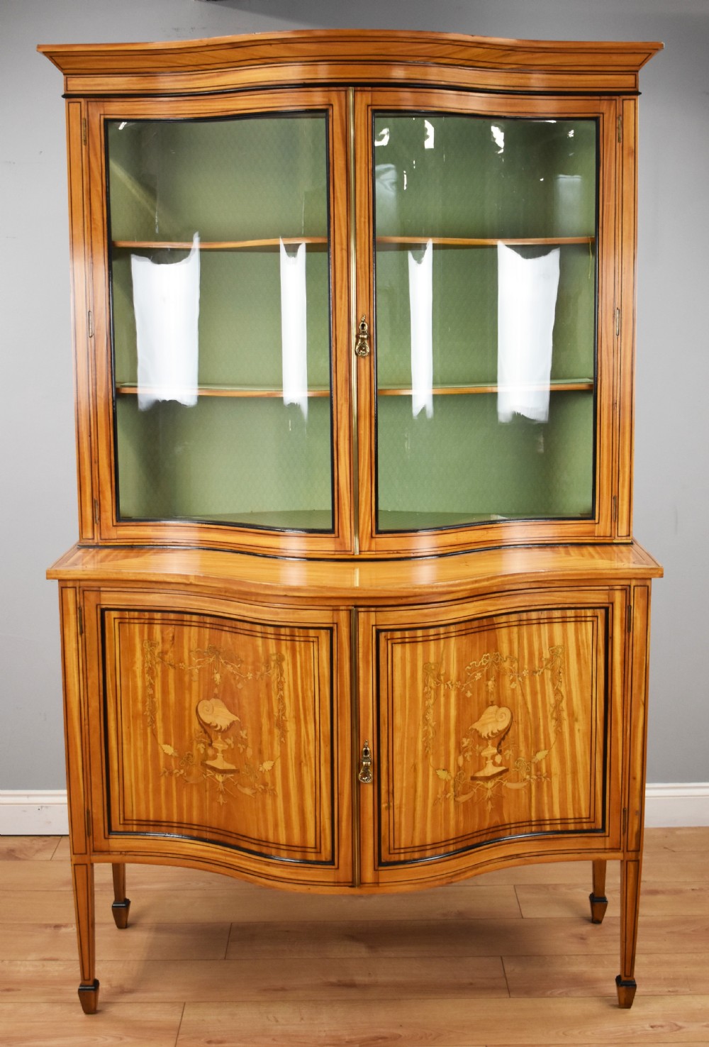A 19th-century satinwood display cabinet featuring a serpentine glazed upper section and inlaid lower cupboard doors. View II