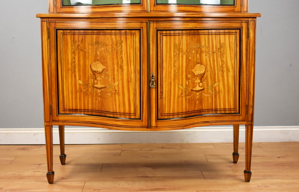 A 19th-century satinwood display cabinet featuring a serpentine glazed upper section and inlaid lower cupboard doors. View IV